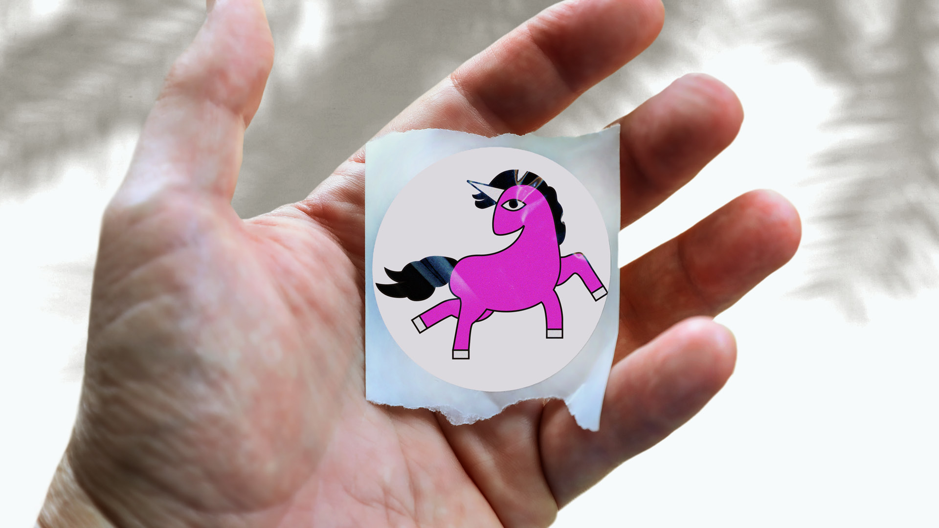 Hand holding a pink unicorn sticker